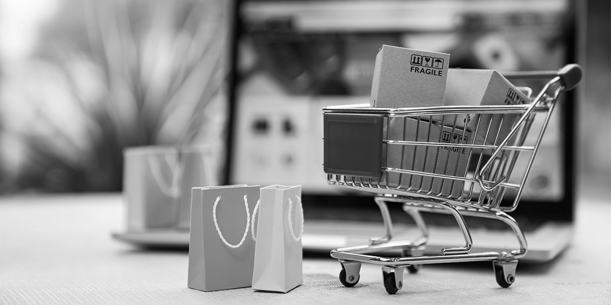 A miniature shopping cart in front of a laptop screen, ecommerce concept